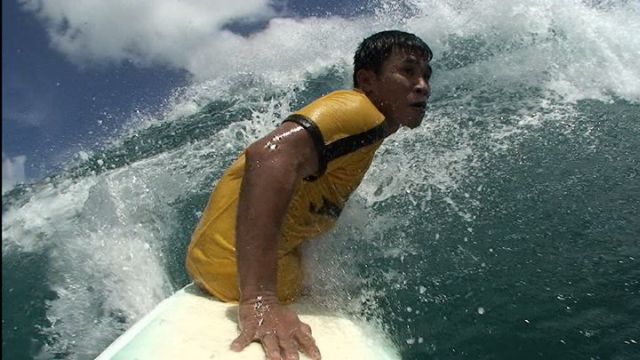 Deddy Dachi s'appuie sur une seule main pour faire le bottom turn sur sa planche de surf.